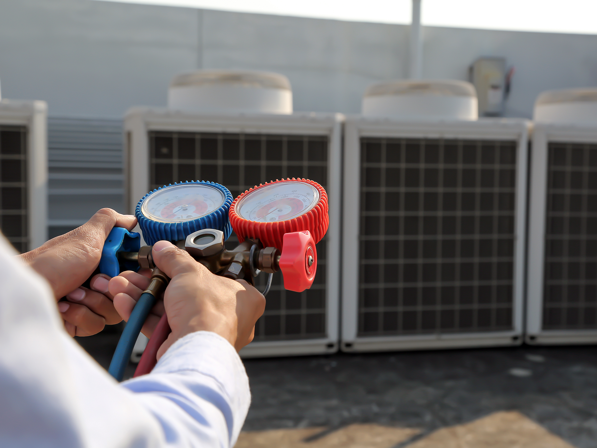Technician using manifold gauge is measuring equipment for filling industrial factory air conditioners and checking maintenance outdoor air compressor unit.