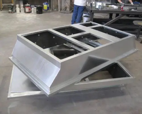 Stacked aluminum vent hoods in an industrial workspace, showcasing a metallic finish and multiple cutouts for ventilation.