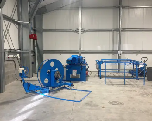 Industrial workshop featuring blue machinery and equipment, including a large spool and a frame, set in a spacious, well-lit area.