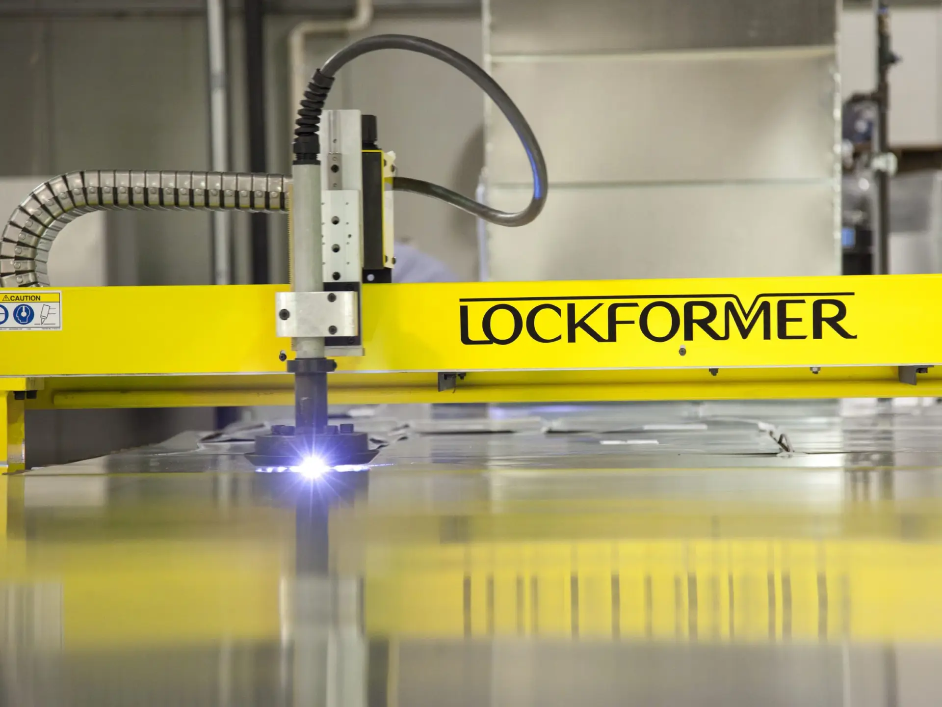 Close-up of a LOCKFORMER machine cutting metal, showcasing a bright cutting tool and industrial setup in a factory environment.